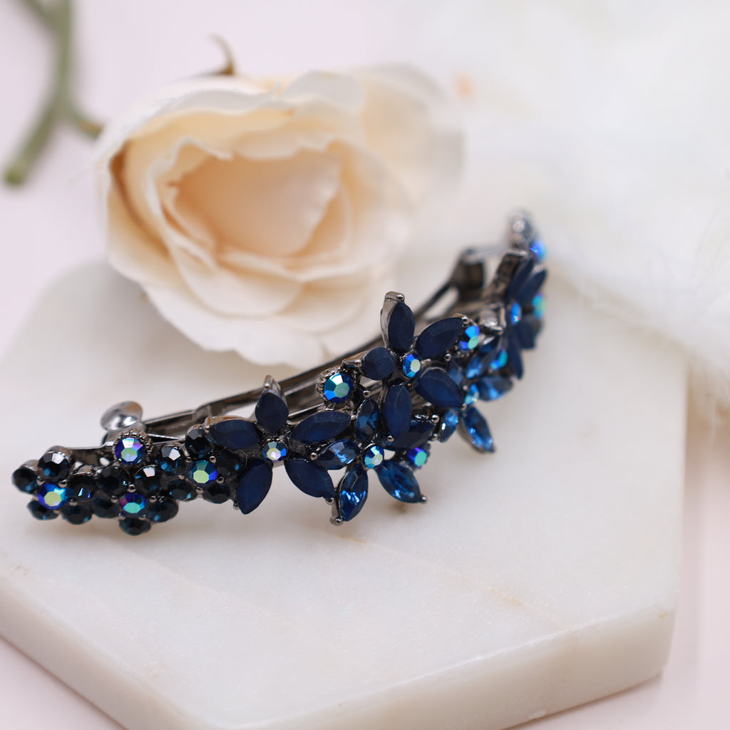Curved gemstone hair barrette in navy blue with floral design, worn on blonde hair against a soft floral background